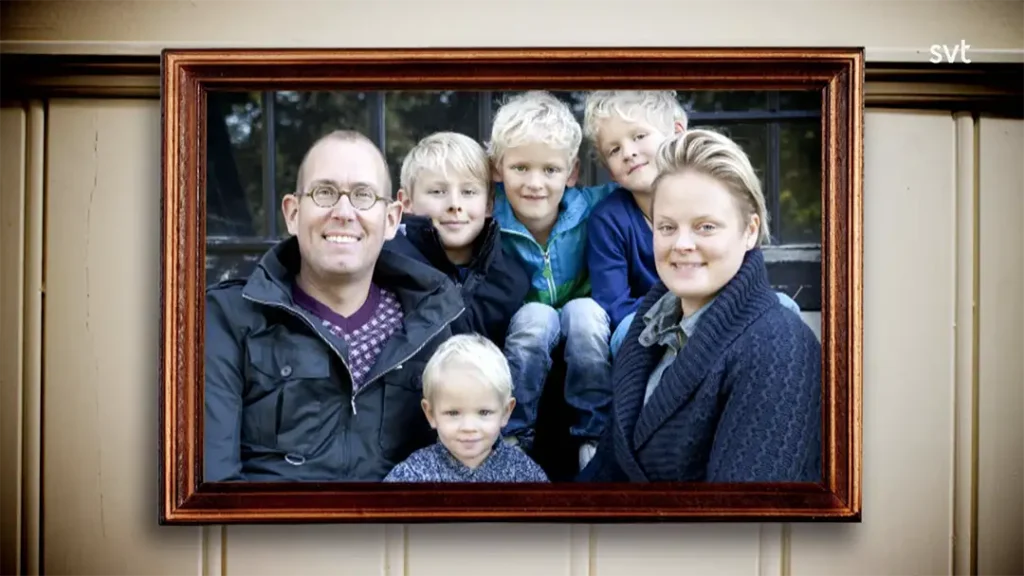 Stiligt - Ett inramat fotografi visar två vuxna och fyra små barn som sitter tillsammans och ler, med en träbakgrund bakom ramen.