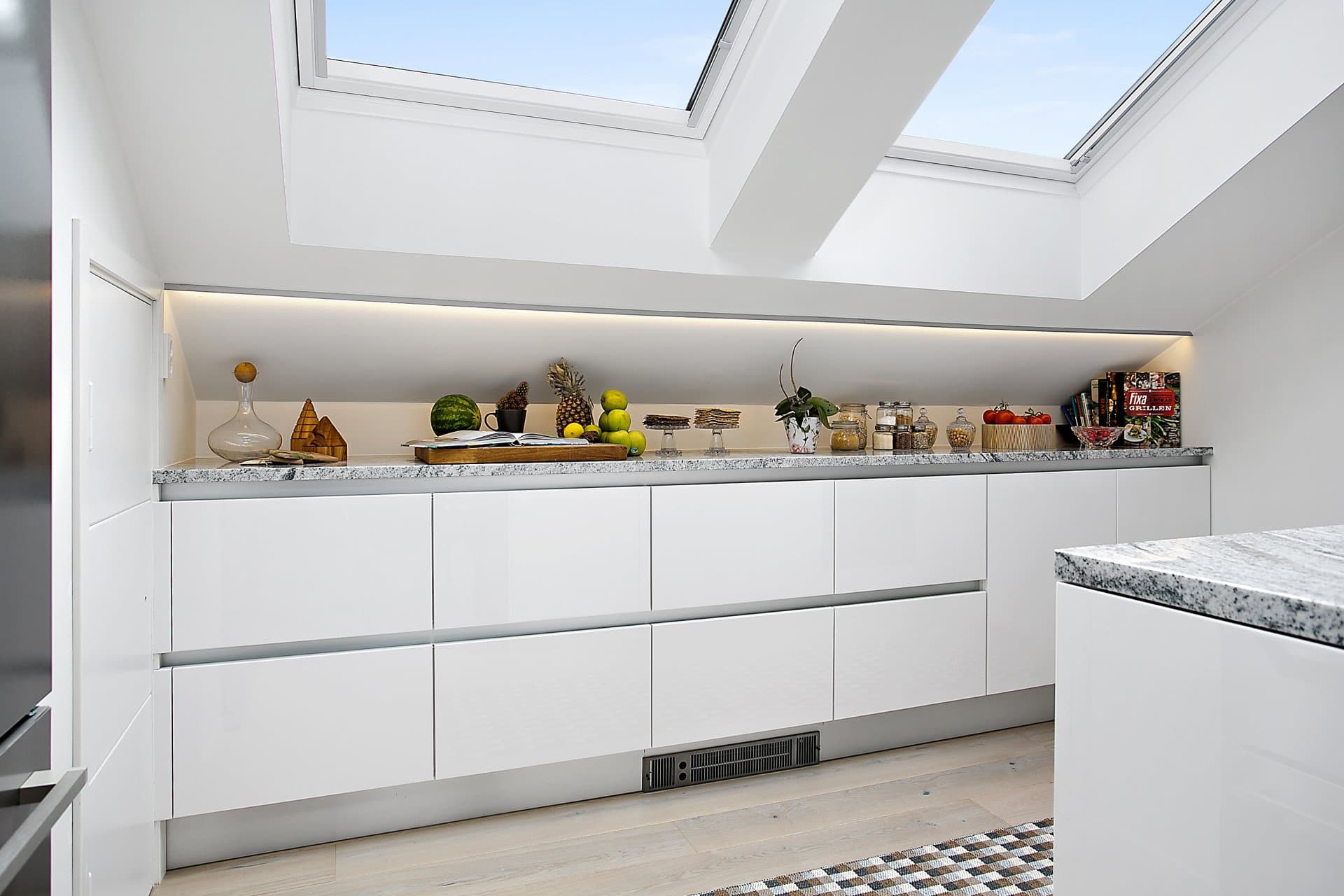 Ett minimalistiskt vitt kök med takfönster i öppen planlösning.