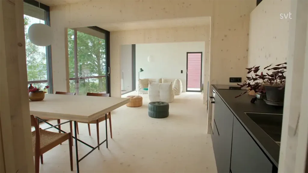 Stiligt - Modernt, minimalistiskt vardagsrum med öppen planlösning inspirerat av Värmland - Husdrömmar, med ljusa trägolv och väggar, ett matbord med stolar, ett kompakt kök och en sittgrupp nära stora fönster.