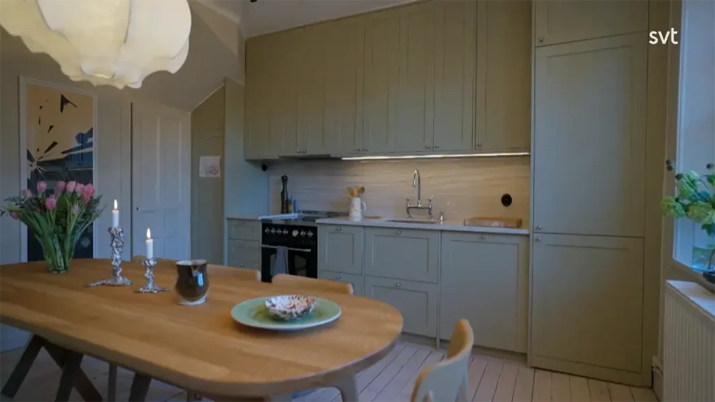 Stiligt - Ett modernt kök i Gamla Enskede - Husdrömmar stil, med ljusgröna skåp, ett matbord i trä med ljus och blommor samt belysning under skåpet ovanför bänkskivan.