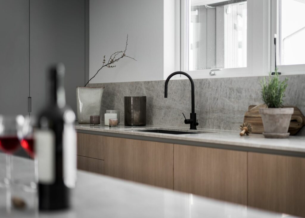 Stiligt - Minimalistiskt kök med stiligt ljusa träskåp, en elegant svart kran, dekorativa växter och en vinflaska elegant placerad på bänken.