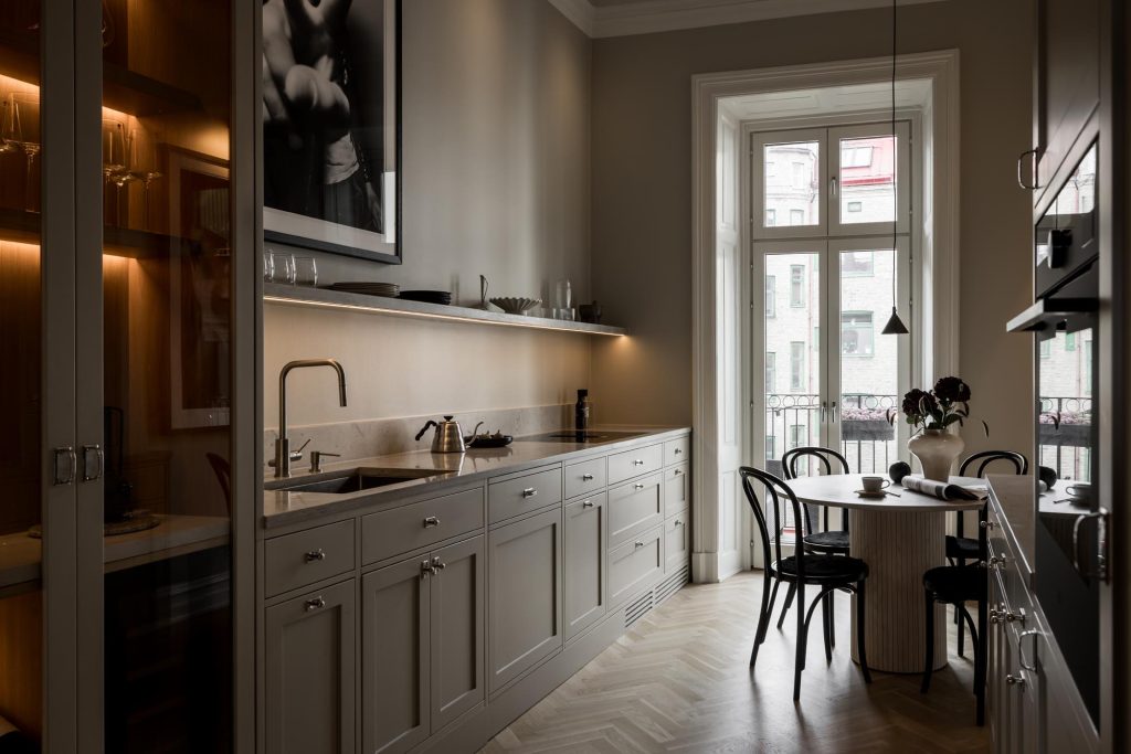 Stiligt - Modern kök i shakerstil med ljusgrå skåp, inbyggda vitvaror, ett litet runt matbordsset för två, stort fönster med utgång till balkong, samt minimalistisk inredning.
