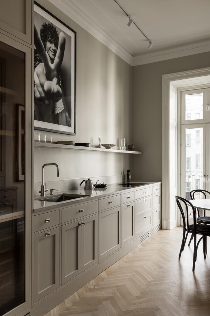 Stiligt - Modernt kök med ljusgrå skåp, snygga bänkskivor och ett inramat svart-vitt foto på väggen. En stilig touch läggs till av det stora fönstret och matsalen med eleganta svarta stolar i bakgrunden.