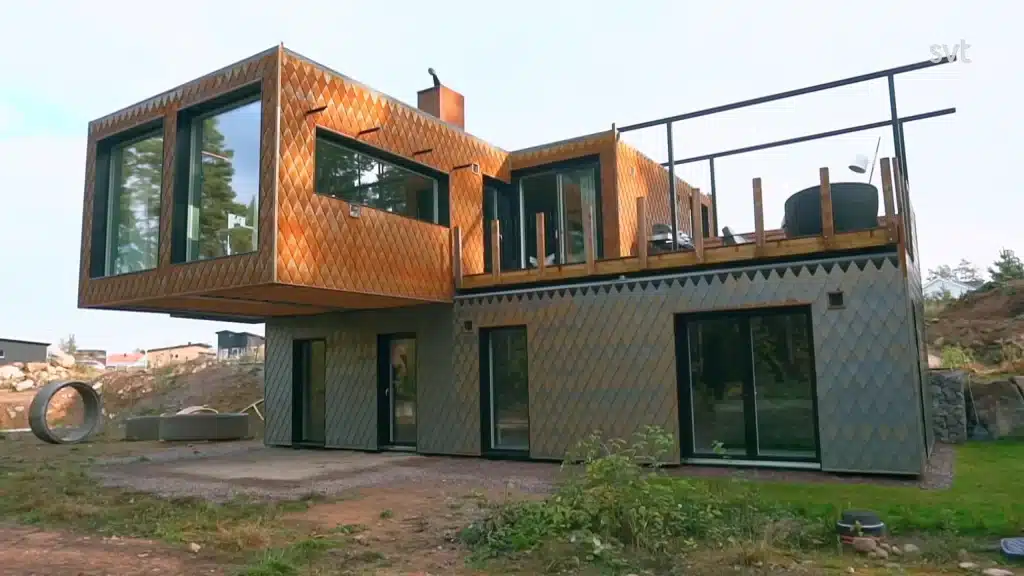 Stiligt - Ett modernt tvåvåningshus med stora fönster och en geometrisk exteriör med metalliska, diamantformade paneler och en fribärande övervåning.